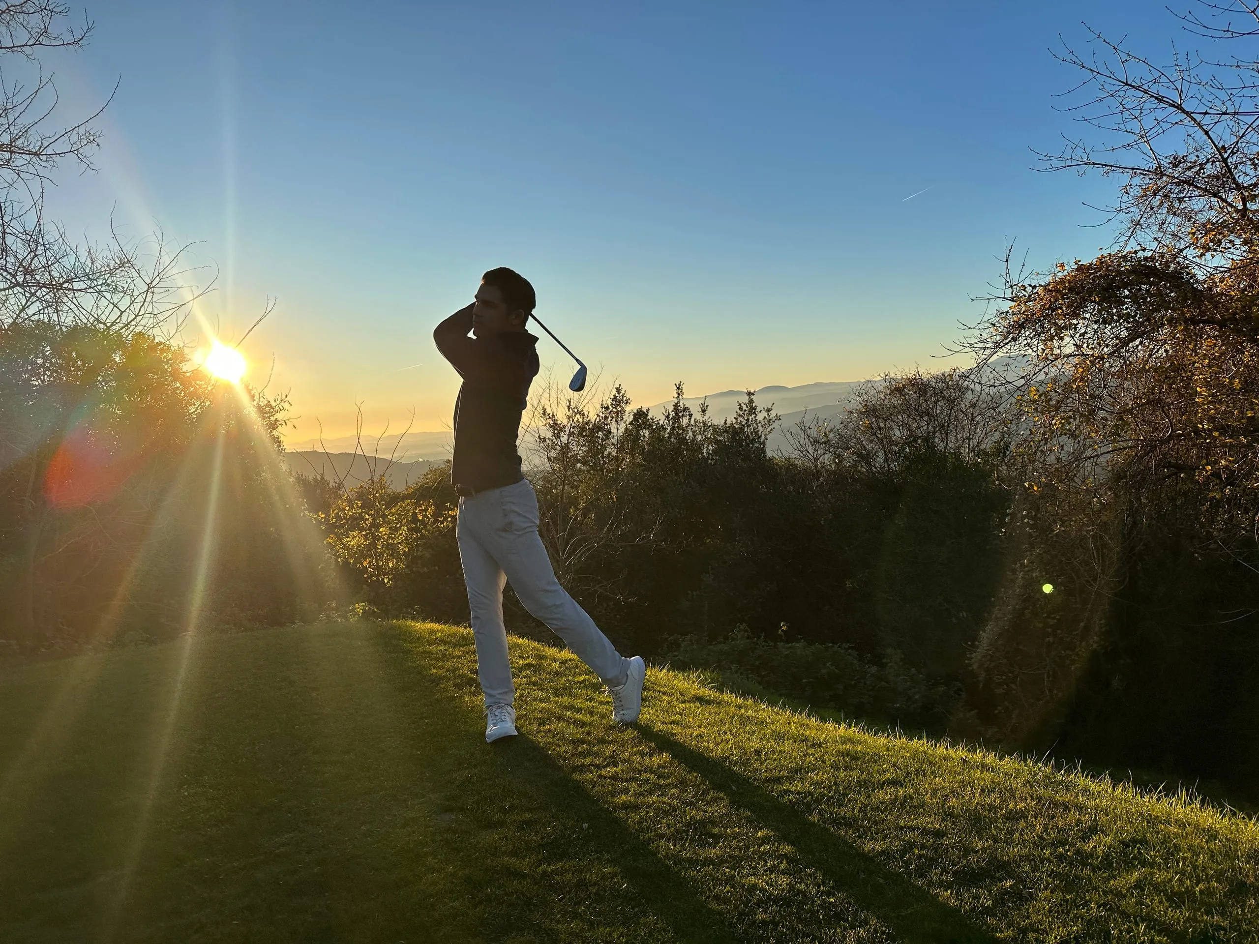 Silhouette of Louis swinging a golf club at sunset